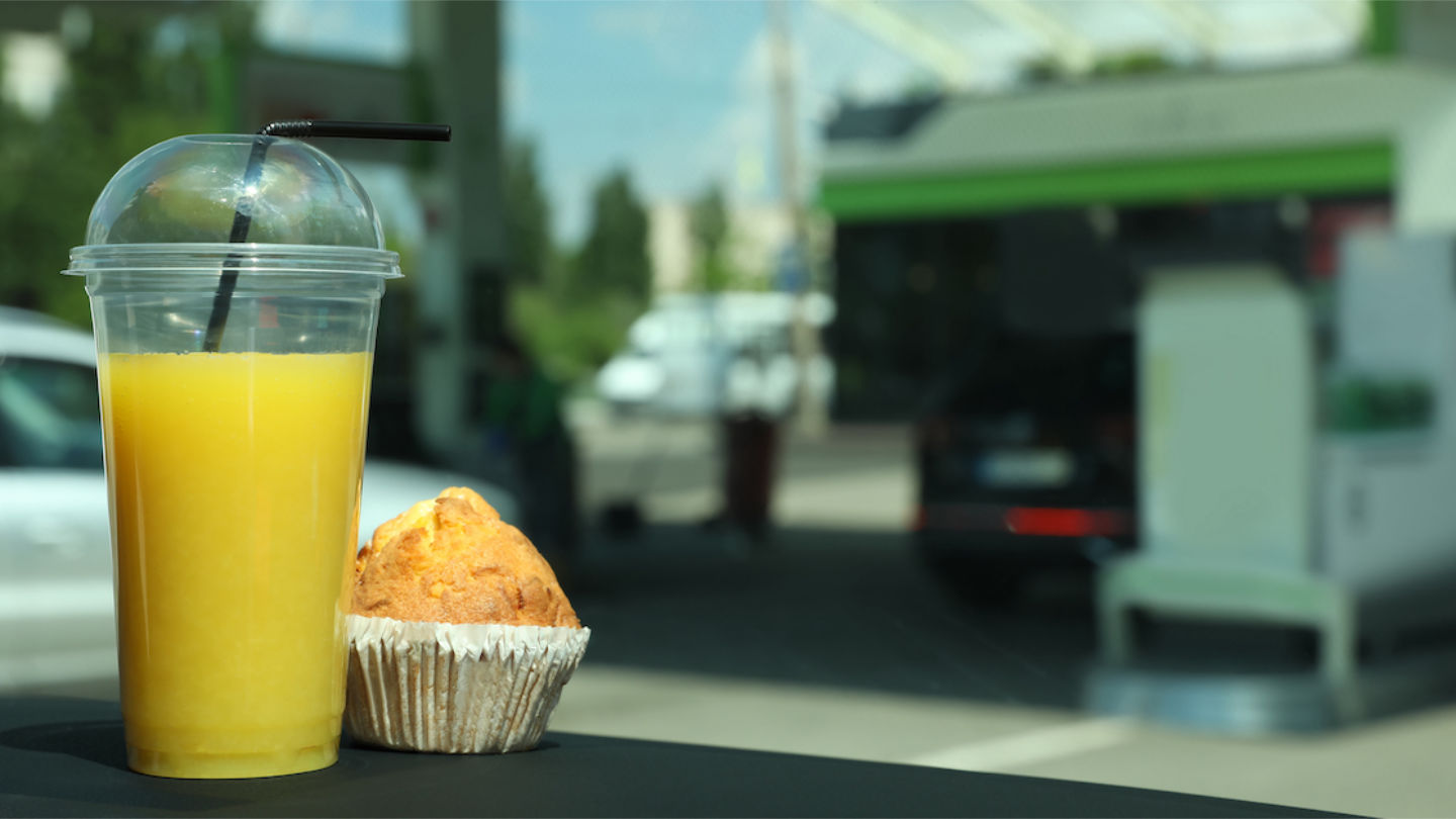Plastic Cup Of Juice And Muffin On Car Dashboard At Gas Station.